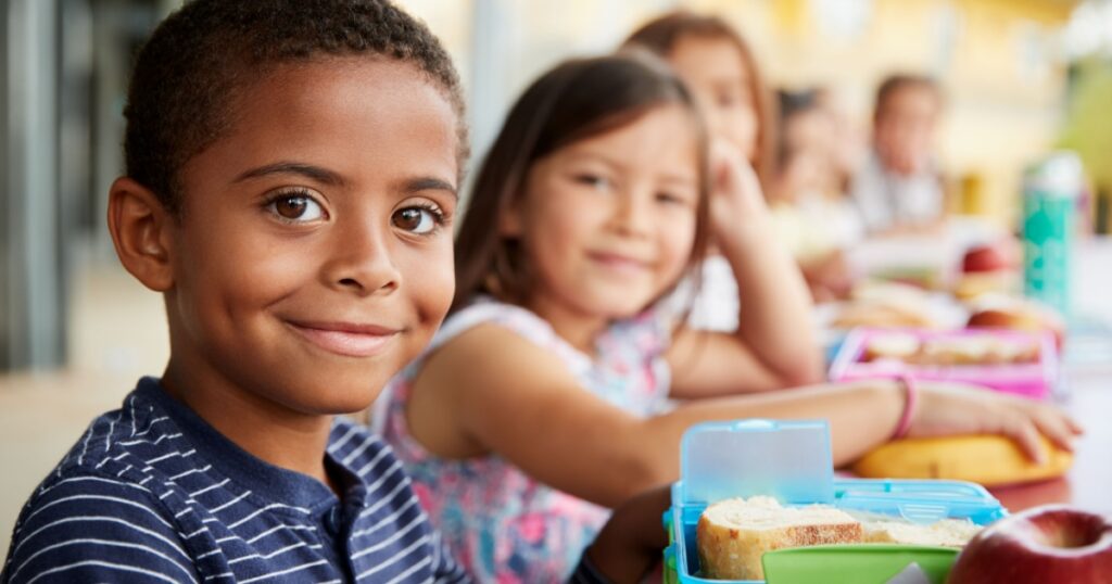 Young boy and girl at school lunch table smiling to camera