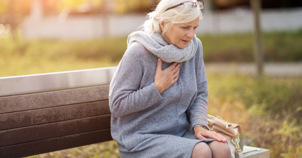 Senior Woman Suffering From Chest Pain While Sitting On Bench