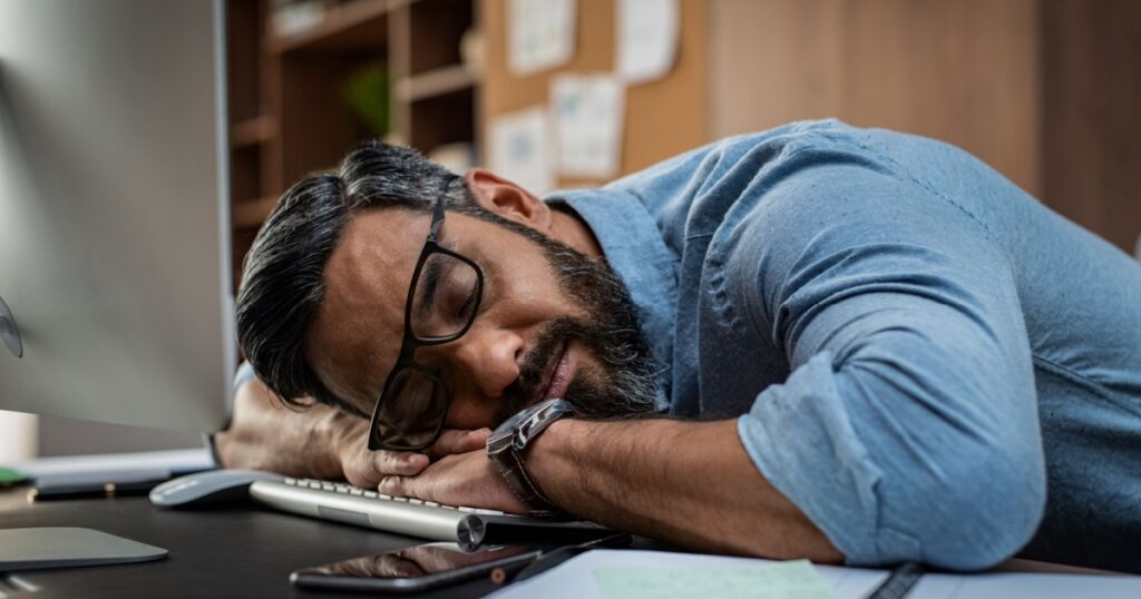 Tired multiethnic businessman sleeping in office. Middle eastern business man with eyeglasses worked late and fell asleep on the computer keyboard. Creative casual man sleeping at his working place