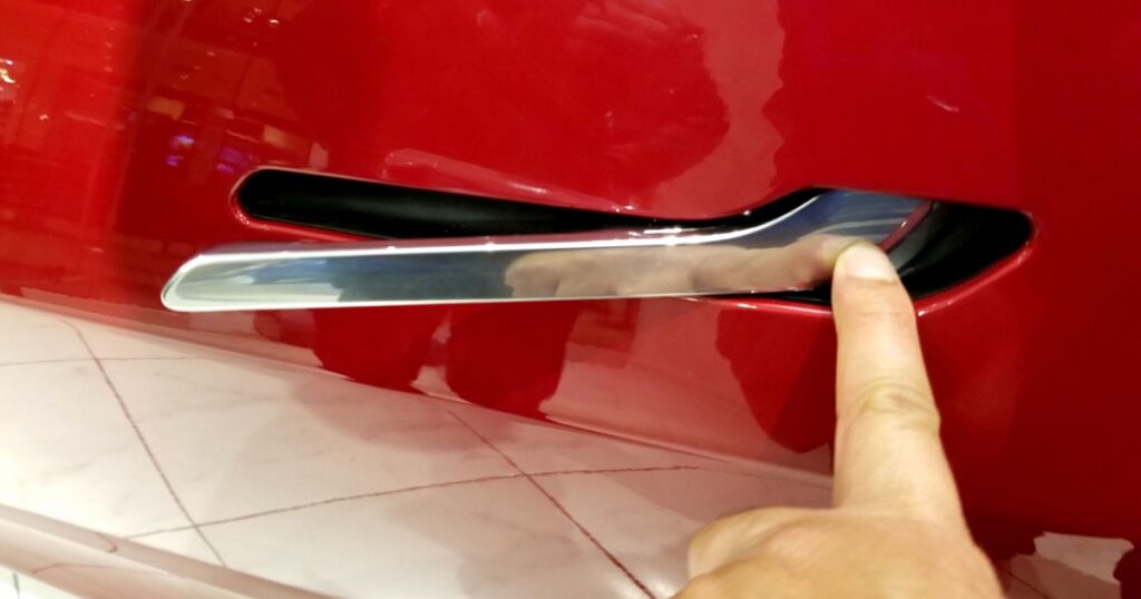 The metal door handle of the red color 2019 Tesla Model 3 all electric sedan