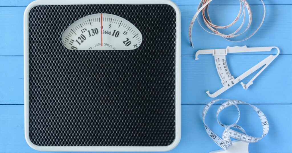 Mechanical weight scale, body mass control concept : Bathroom scale, personal accurate body fat tester / skin fold caliper measurement tool for stomach / belly and measuring tape on blue background