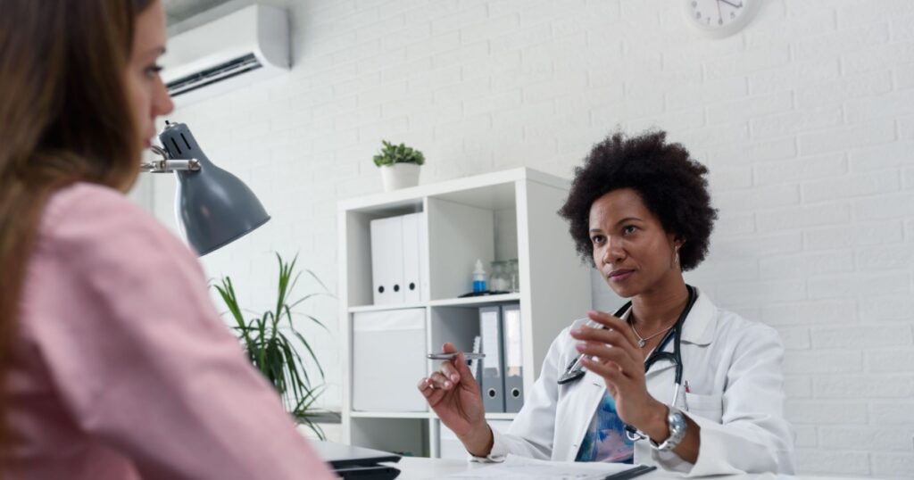 A female doctor sits at her desk and chats to a female patient while looking at his test results