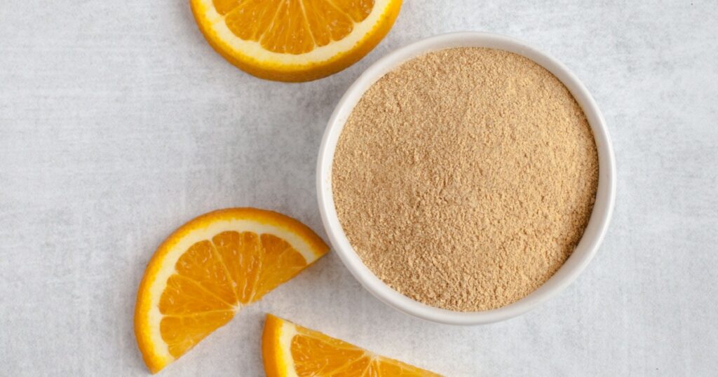 Orange peel powder in white bowl with orange slices on light grey background