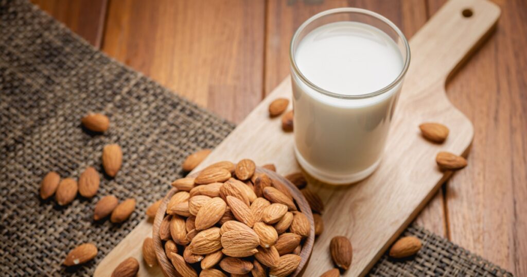 Almond milk in the glass with almond in the wooden bowl on the wooden table.