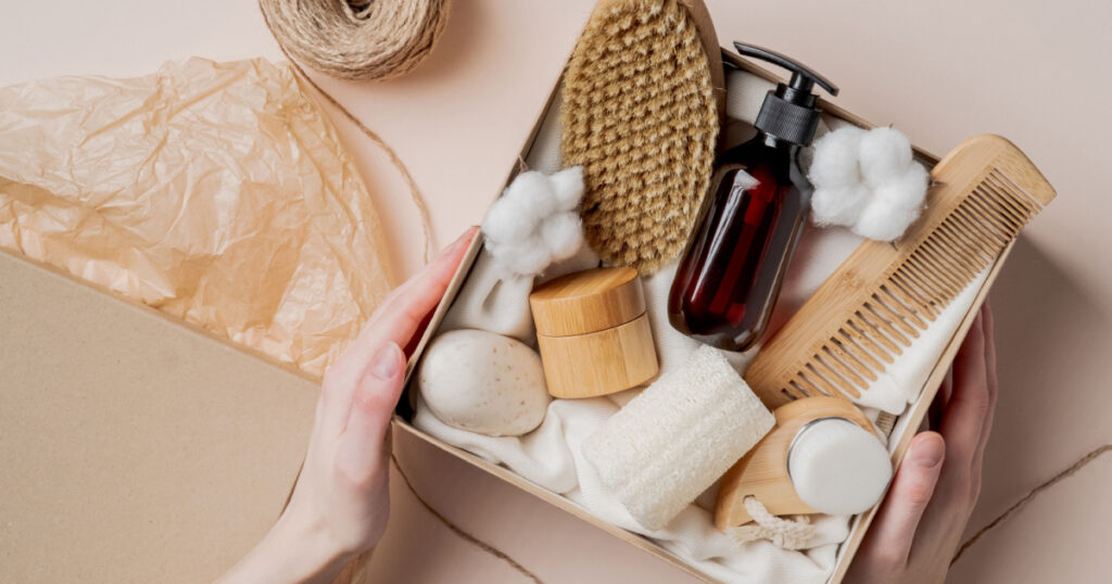 Beauty subscription Box preparation. Female hands holding gift box with natural skincare products, body brush, shampoo, soap, moisturizer.