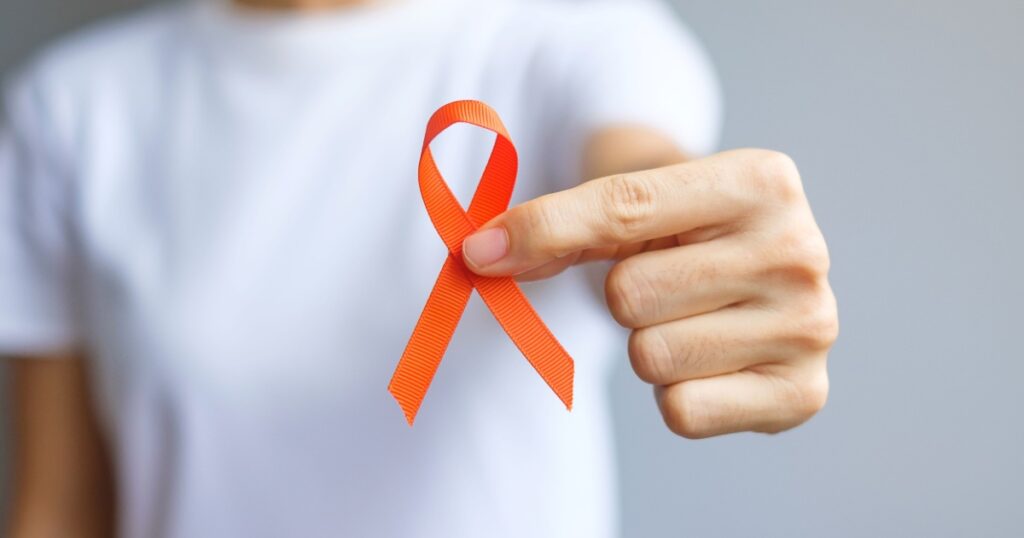 hand holding Orange Ribbon for Leukemia, Kidney cancer day, world Multiple Sclerosis, CRPS, Self Injury Awareness month. Healthcare and word cancer day concept