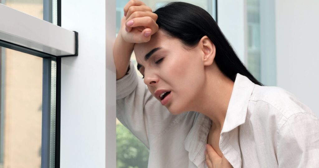 Young woman suffering from breathing problem near window indoors
