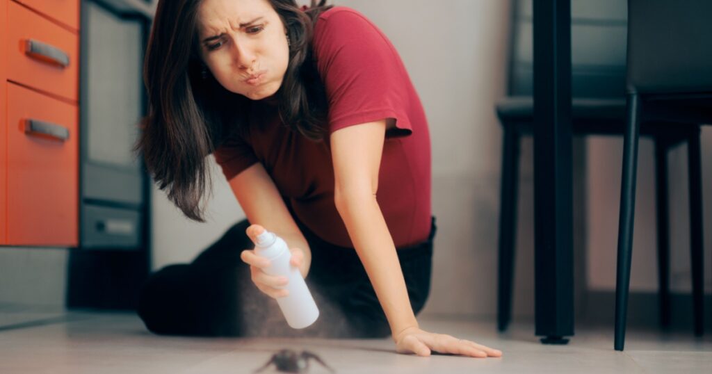 Woman Spraying with Insecticide Over an Ant on the Kitchen Floor. Homeowner dealing with pest infestation problem in her own apparent