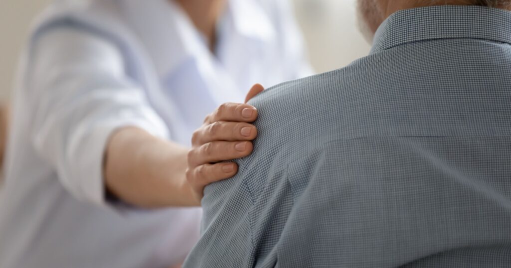 Close up caring doctor touching mature patient shoulder, expressing empathy and support, young woman therapist physician comforting senior aged man at meeting, medical healthcare and help