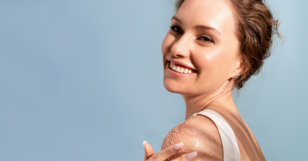 A beautiful tender woman put a natural cosmetic scrub to her shoulder and smiles