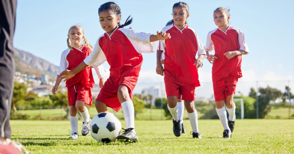 Soccer, ball or sports and a girl team training or playing together on a field for practice. Fitness, football and grass with kids running or dribbling on a pitch for competition or exercise
