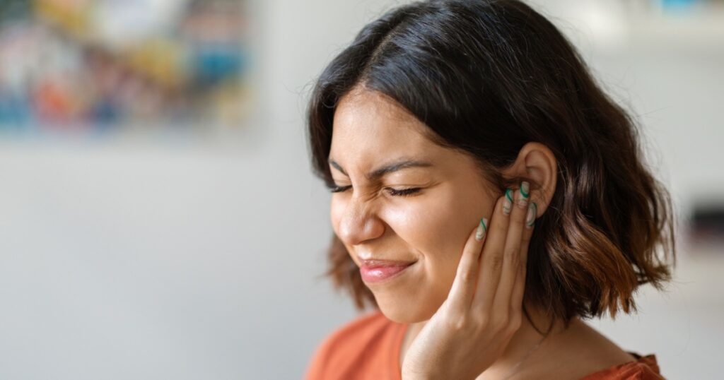 Sick young arab woman having ear pain at home, upset middle eastern female rubbing sore auricle with hand and frowning, suffering from otitis and acute ache, closeup shot with copy space