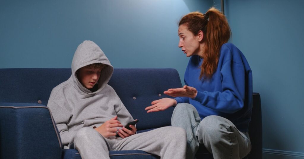 Mom screams and scolds her son in the room on the blue sofa. Irritated woman teaches a lesson to a teenager. The boy has a difficult adolescen