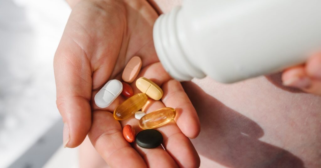 Closeup photo of supplements with a white bottle. Pregnant woman take omega 3, multivitamins, vitamins B, C, D, collagen tablets, probiotics, iron capsule. Girl hold vitamins daily. Top view.