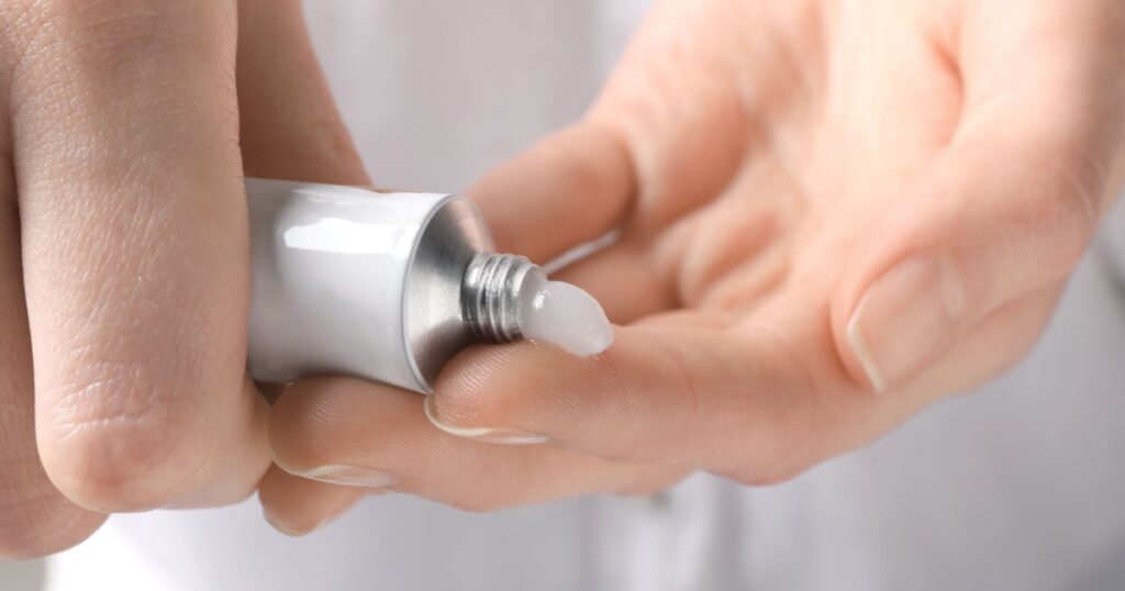 Woman squeezing out ointment from tube on her finger, closeup