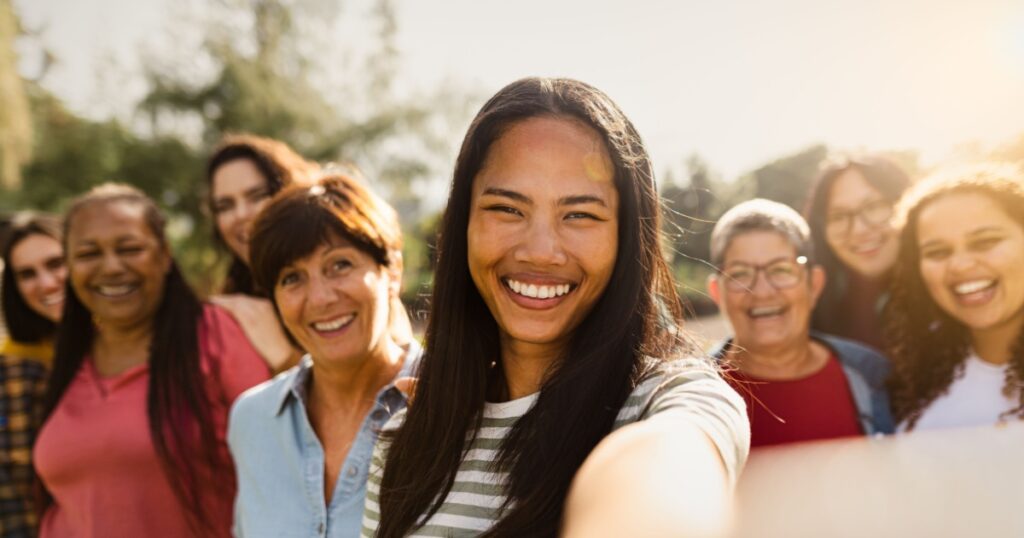 Happy multigenerational group of women with different ethnicities having fun taking selfie with smartphone camera in a public park - Females empowerment concept