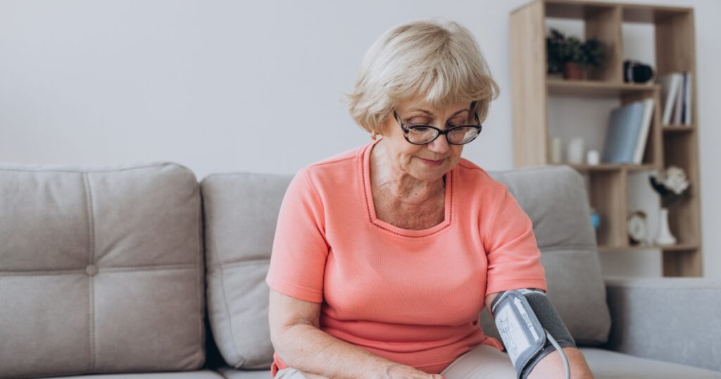 Senior woman with hypertension measuring blood pressure herself at home. Sad Mature lady measure blood pressure using tonometer. Everyday health check-up