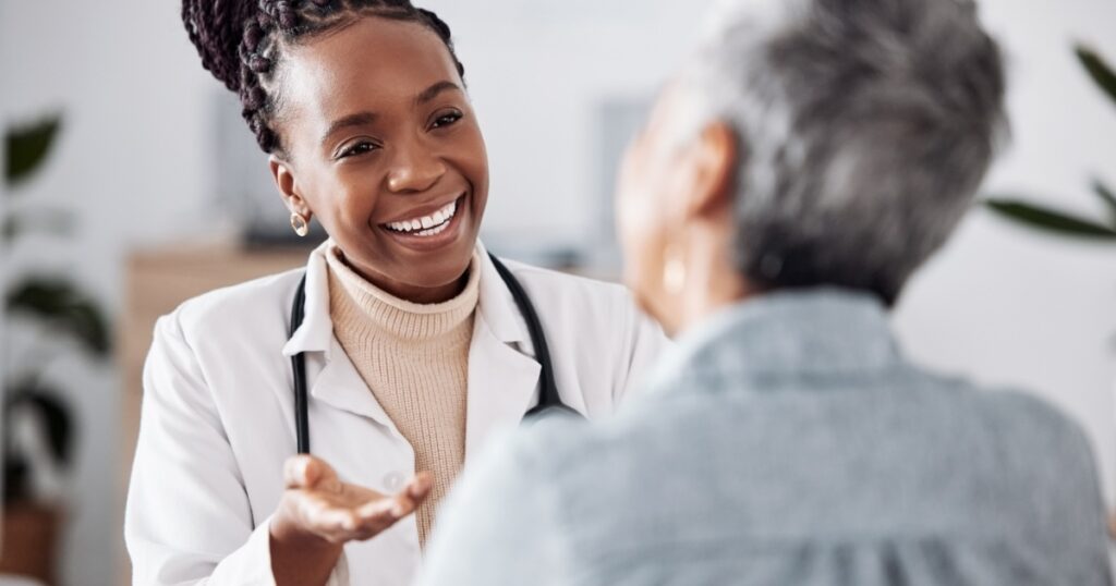 Smile, black woman or doctor consulting a patient in meeting in hospital for healthcare feedback or support. Happy, medical or nurse with a mature person talking or speaking of test results or advice