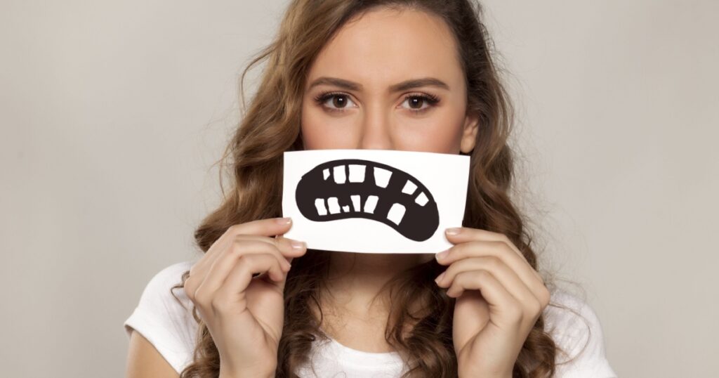 sad girl with a defective teeth painted on paper over her mouth