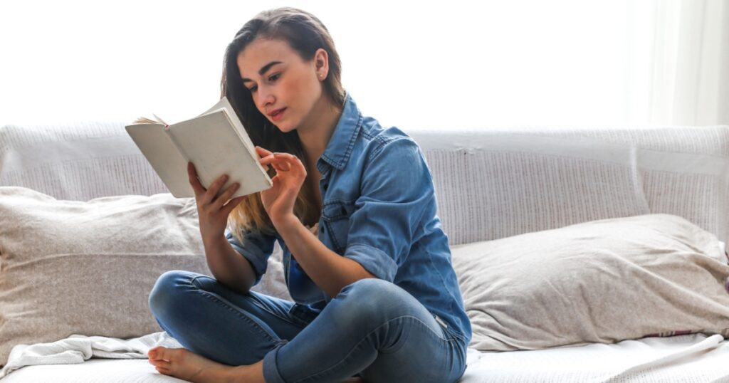 White cozy bed and a beautiful girl, reading a book, concepts of home and comfort, place for text