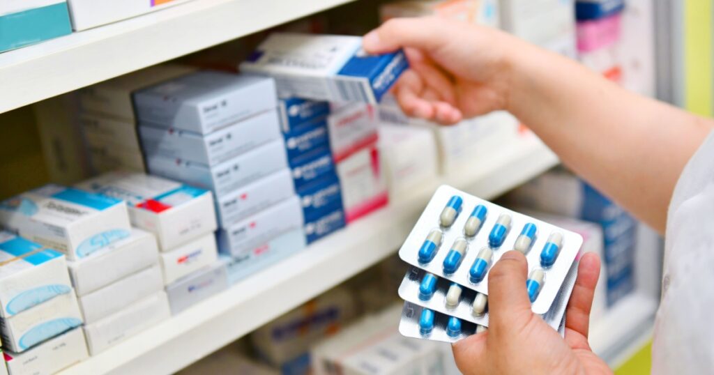 Pharmacist holding medicine box and capsule pack in pharmacy drugstore.