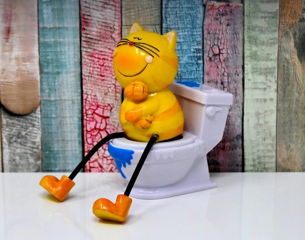 Toy cat sitting on fake toilet. Quirky and colorful wood panels in the background.
