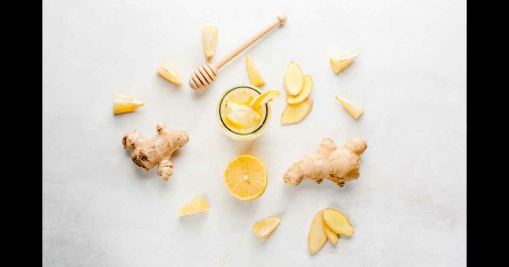 Ginger-lemon drink in a bottle with a straw. Selection of the ingredients of ginger cocktail or tea: ginger root, lemon, honey. On white table. Top View,copy space
