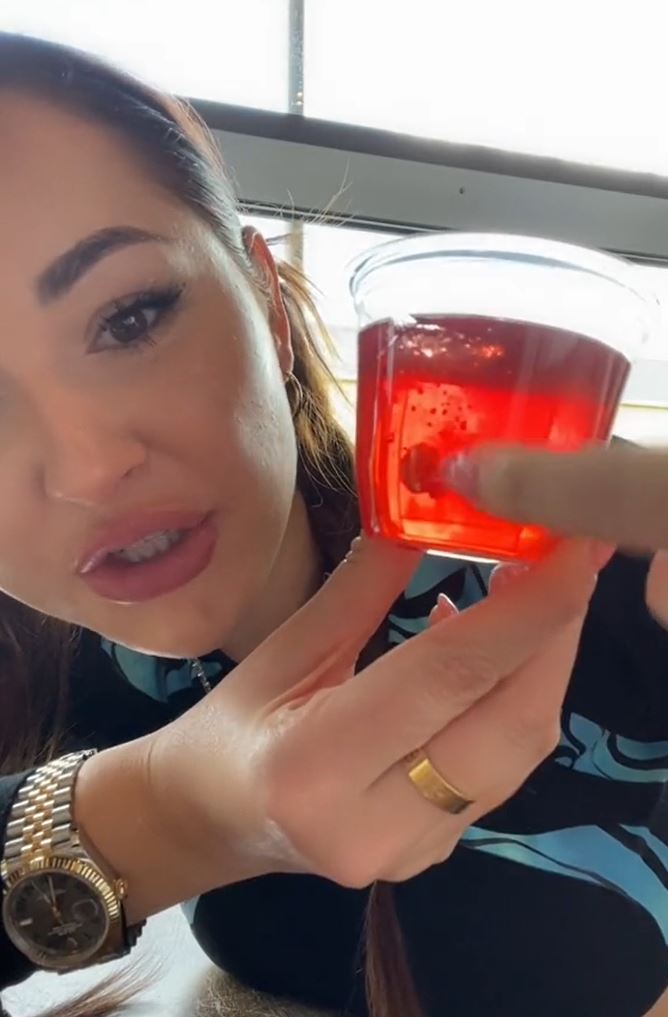 A woman pointing to a red Jello cup. Windows in the background. 