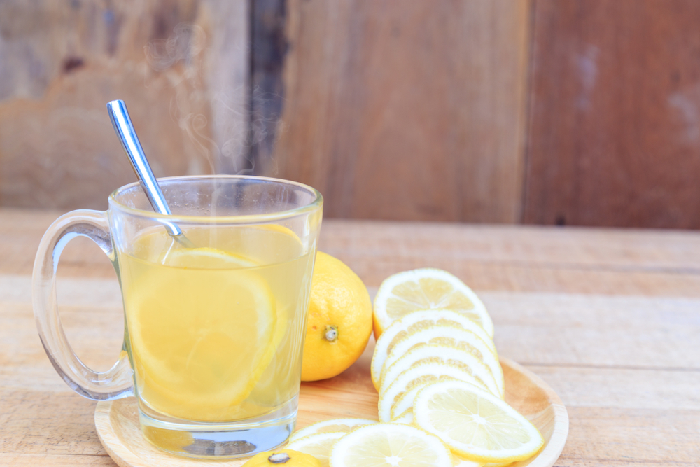 Drinking hot lemonade drink helps to heal the sick or cough or cold from the cold air in a glass with a spoon and slices of lemon on a natural wooden table with copy space.