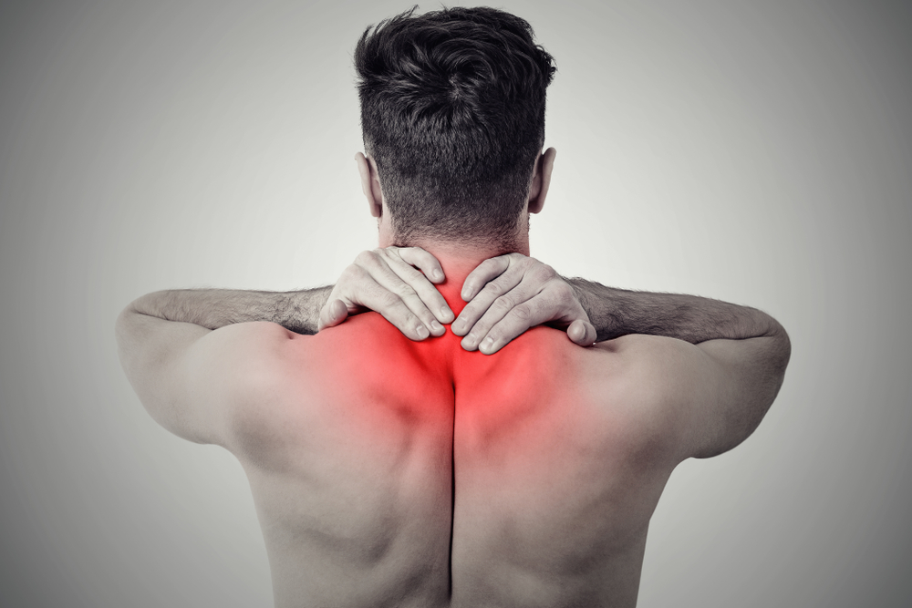 Black and white shot of man from back having red spot of pain and trauma in neck.
