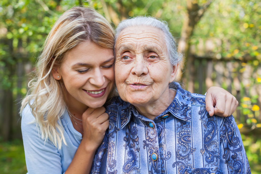 Young attractive woman embracing old grandmother outdoor. Female - generations - love
