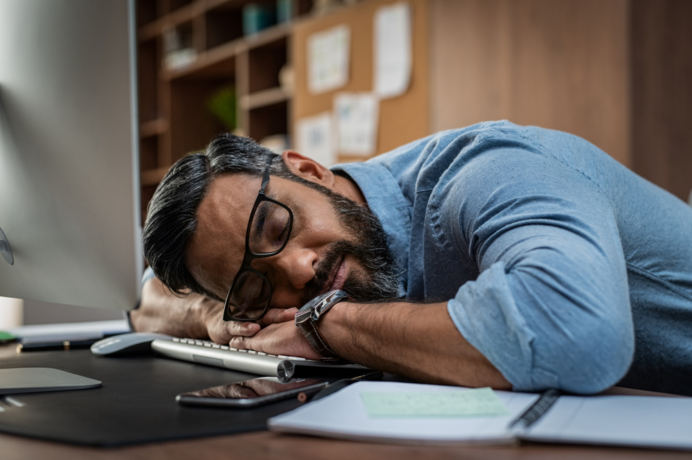 Tired multiethnic businessman sleeping in office. Middle eastern business man with eyeglasses worked late and fell asleep on the computer keyboard. Creative casual man sleeping at his working place