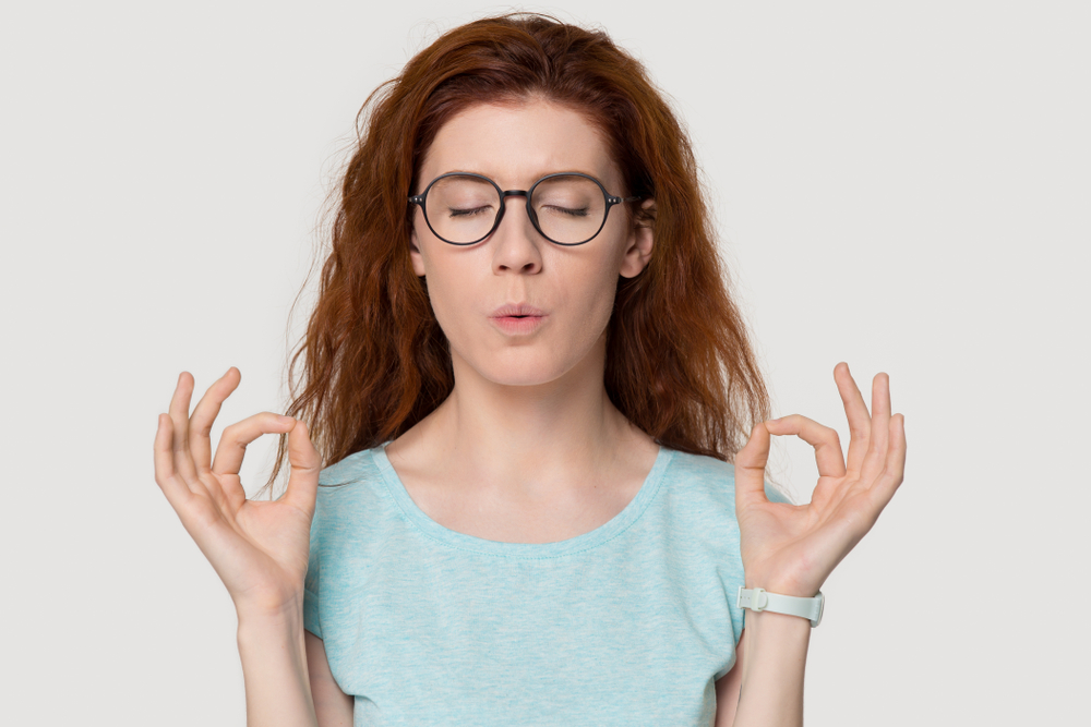 Stressed redhead woman meditating relieving managing stress doing yoga breathing exercises calming down, nervous red-haired lady exhaling self-soothing isolated on white grey studio blank background
