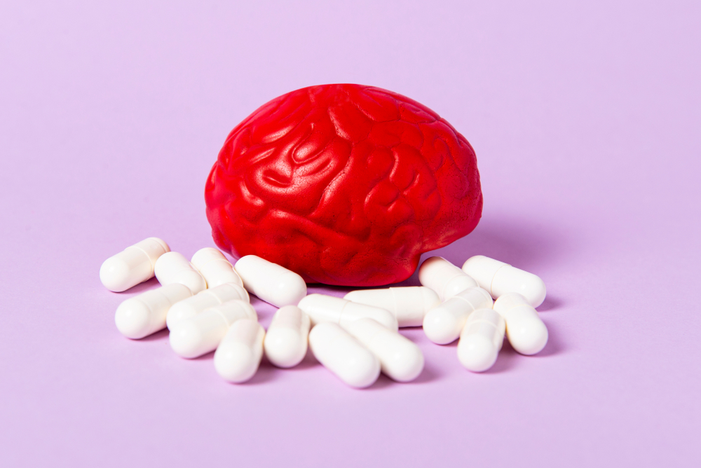 Red brain on a pink background with white pills. Some pills for the brain. Symbolic for drugs, psychopharmaceuticals, nootropics and other drugs. The medicine. Brain treatment