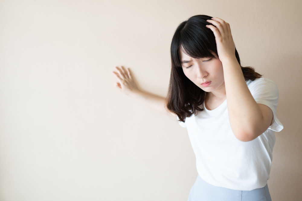 Young asian female suffering from dizziness, vertigo and headache over white background. Cause of dizzy inclued migraine, stress, stroke, BPPV, Meniere’s disease or brain tumor. Health care problem.