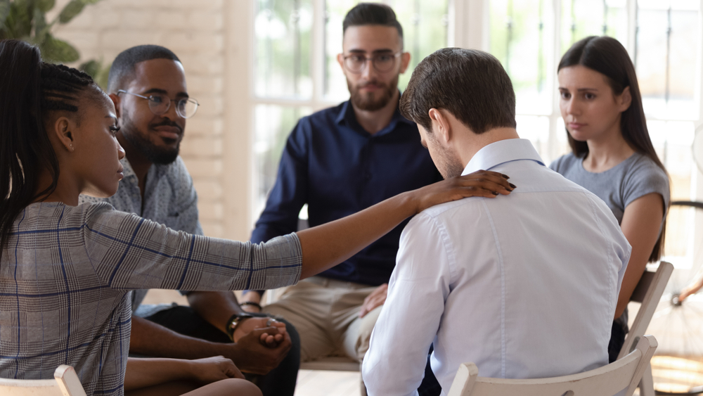 Rear view at upset man feel pain depression problem addiction get psychological support of counselor therapist coach diverse people friend group help patient during therapy counseling session concept