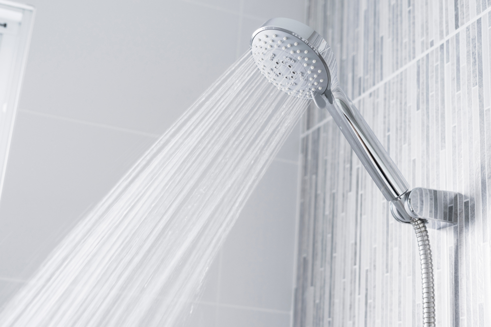 Fresh shower behind wet glass window with water drops splashing. Water running from shower head and faucet in modern bathroom.