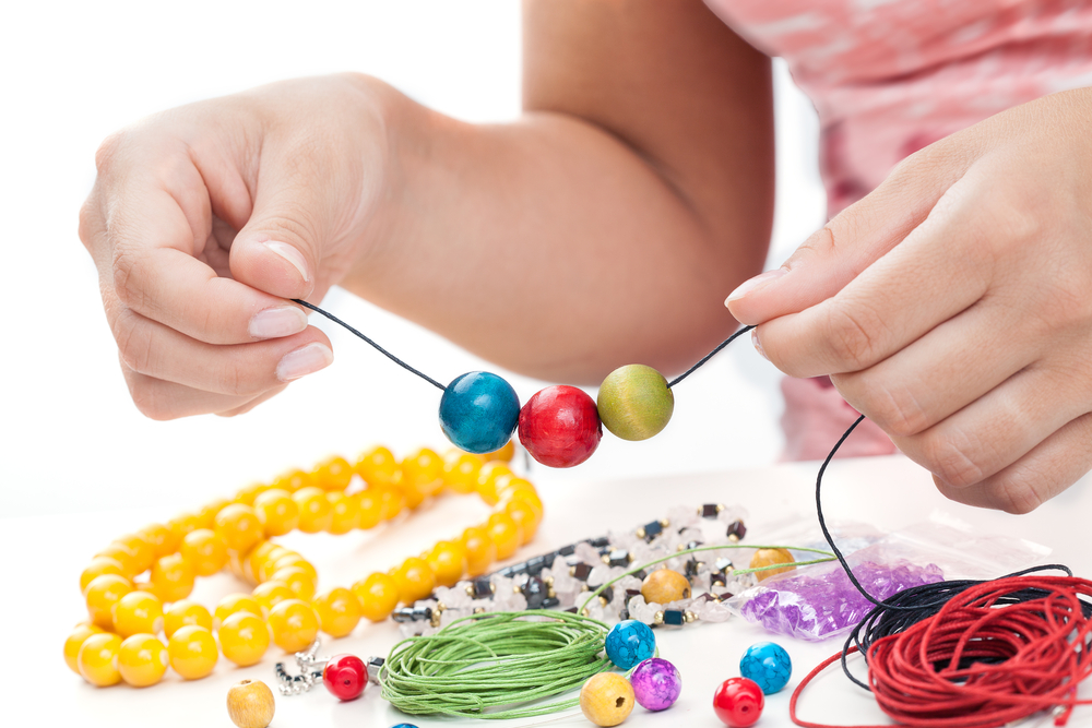Girl's hands making a necklace with wooden beads