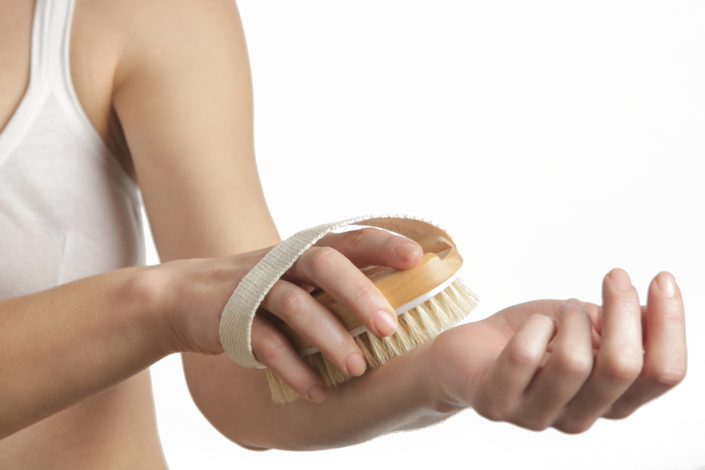 Dry body brush, Woman dry brushing body to reduce cellulite, detoxify the lymphatic system, and achieve beautiful smooth skin. Dry skin brushing as part of morning health and energy routine.