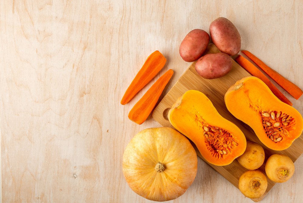 two pieces of sliced pumpkin and carrot, round pumpkin, potato, turnip and garlic are laid out on a bamboo cutting Board and a light wooden background, top view, space for text, flat lay food