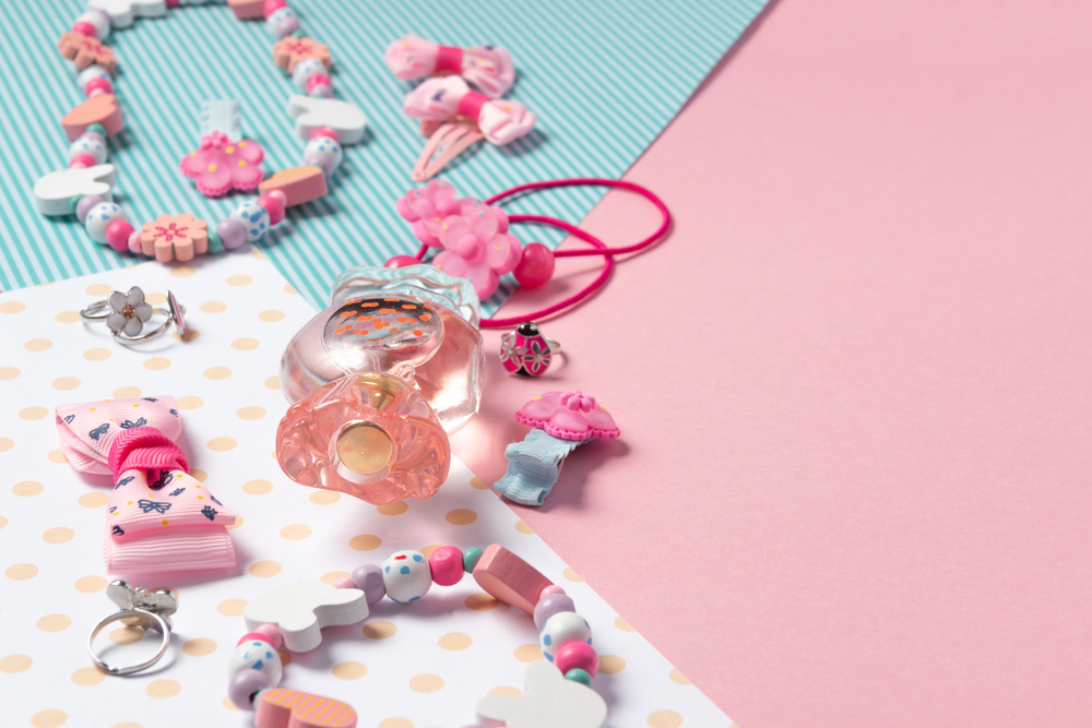 Children's flat lay. Perfume in the form of candy, children's jewelry and hair accessories on a pink background. Accessories for little girls