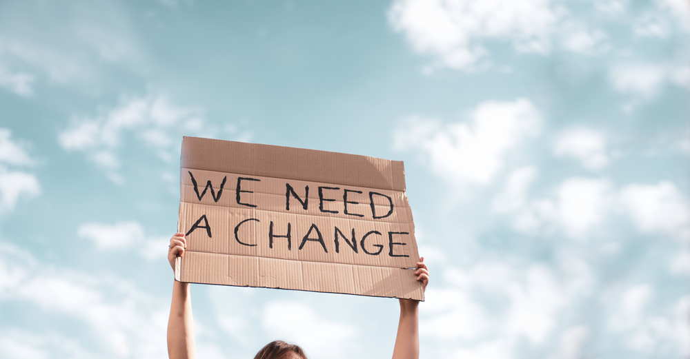 Group of activists with banners protesting over pollution and global warming. Male and female rebellions doing a silent protest to save a planet earth. Woman holding a banner of 'We Need A Change'.