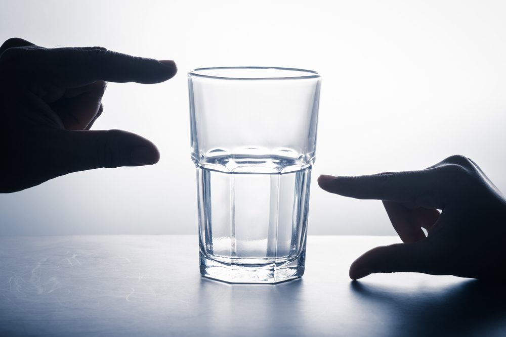 Hands measure on glass that has an empty part and left water, glass half full attitude concept, crisis and opportunity point of view