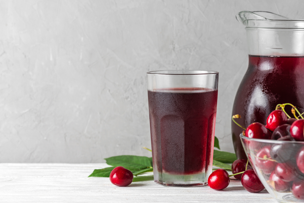 Cherry juice in a glass and jug with fresh berries on white background. Refreshment summer drink. Healthy drink