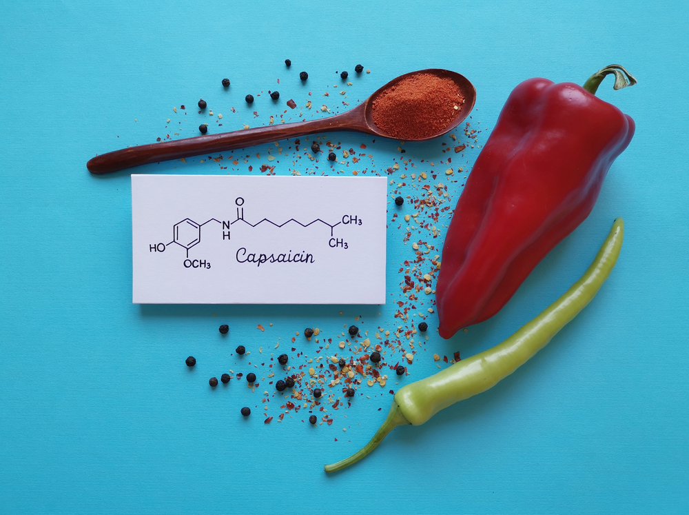 Structural chemical formula of capsaicin molecule with chili peppers, chili powder, and peppercorns. Capsaicin is the compound found in chili peppers that gives them their hot and spicy kick.