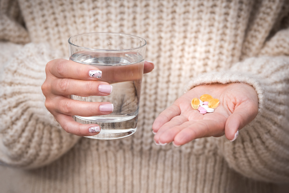 Woman hands holding glass of water, vitamins and supplements. B12, D3, selenium. Vitamins for vegans.