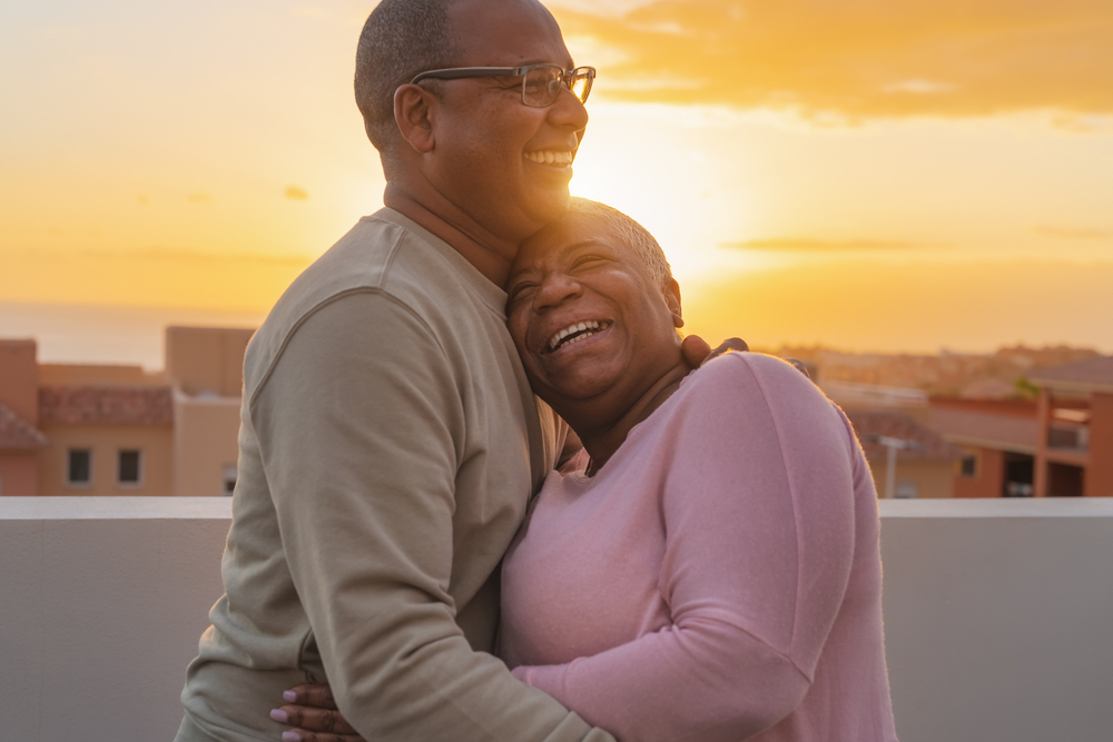 Happy Latin senior couple having romantic moment embracing on rooftop during sunset time - Elderly people love concept
