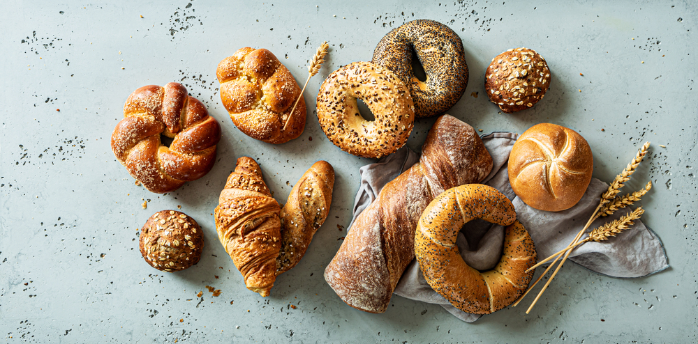 Bakery - various kinds of breadstuff. Bread rolls, bagel, sweet bun and croissant captured from above (top view, flat lay). Grey stone background.