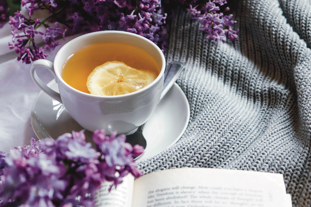 Spring composition flat lay with white cup of lemon tea, beautiful bouquet of lilacs, sweater. Concept of spring and comfort. Still life spring photography for card, poster, banner, wallpaper.