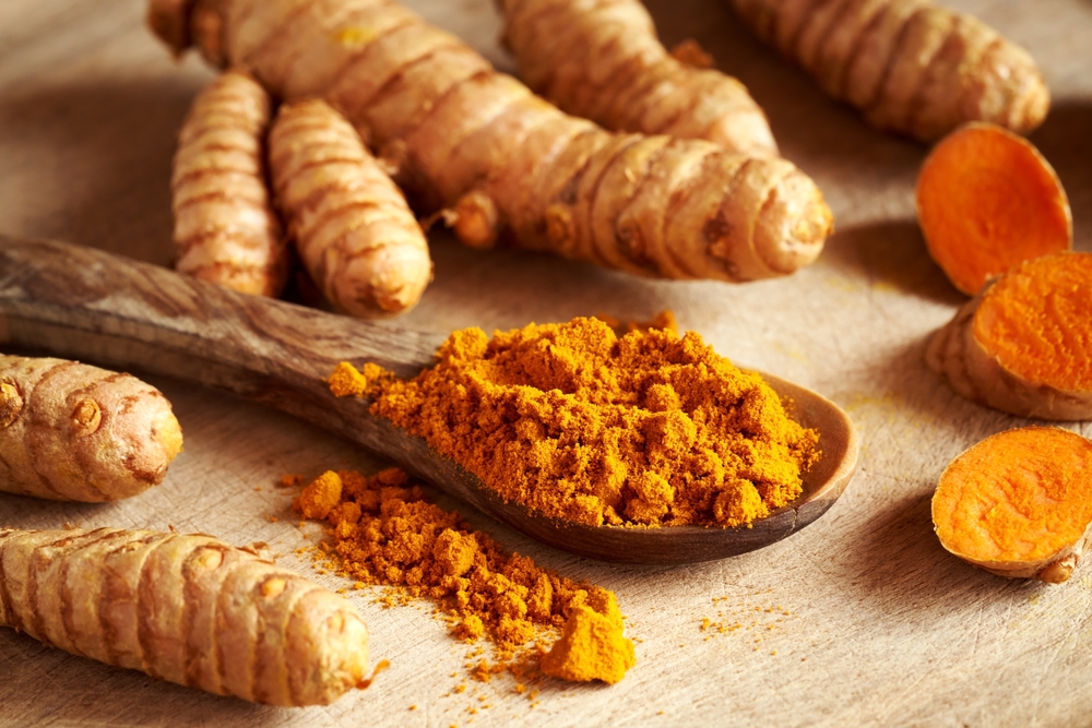 Turmeric powder on a wooden spoon with fresh whole and sliced root in the background